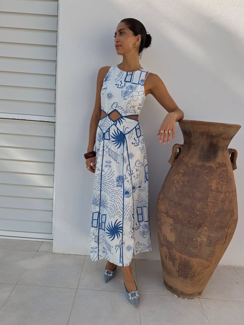 Rochie albă cu imprimeuri botanice albastre, detaliu decupat și o siluetă fluidă. Asortată cu pantofi ascuțiți de culoare albastru deschis, împodobiți cu o piatră prețioasă.