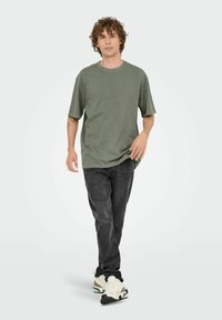 Olivengrøn, kortærmet t-shirt med rund hals, båret med slidte sorte jeans og multifarvede sneakers med beige og grønne accenter.
