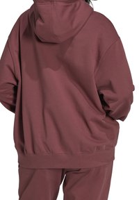 Felpa oversize in misto cotone bordeaux, presenta un cappuccio con coulisse, polsini e orlo a coste, con una texture morbida e liscia.