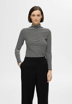 Stribet sort-hvid turtleneck top med lange ærmer, parret med løstsiddende sorte bukser. Glat tekstur og tætsiddende design.