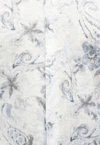 Λευκό ύφασμα με ανοιχτό γκρι και μπλε λουλουδάτα και στροβιλιστά μοτίβα, με τρία ορατά λευκά κουμπιά στο κέντρο.