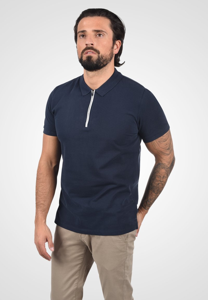 Navy kortermet polo-skjorte med glidelåskrage og en tettsittende design, laget av myk bomullsblanding.