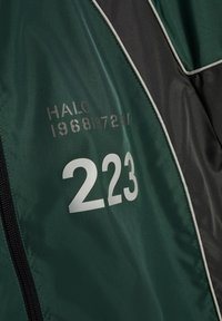 Dunkelgrüner und schwarzer Stoff mit weißer Zahl "223" und verblasstem Text "HALO 1968 1972" darauf gedruckt.