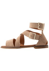 Sandalias de ante con tira al tobillo en marrón claro, con tiras cruzadas y hebillas de metal cuadradas, que cuentan con una suela plana y diseño de punta abierta.