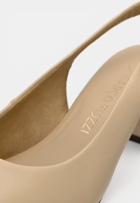 Escarpin beige à finition mate lisse, avec un design à bride arrière et un intérieur rembourré. Logo doré embossé sur la semelle intérieure.