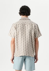 Short-sleeve shirt in a patterned fabric featuring brown and cream geometric shapes, with a collar and a relaxed fit. Cotton blend material.
