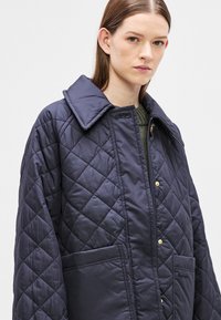 Ναυτικό μπλε μπουφάν με καπιτονέ ύφασμα, μεγάλο γιακά, κλείσιμο με κουμπιά τύπου snap και δύο μπροστινές τσέπες με απαλή υφή. Διακριτό διαμάντι σχέδιο σε όλο το μπουφάν.