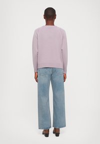 Lavender crewneck sweater with ribbed hem and cuffs, paired with light blue wide-leg jeans and black heeled shoes, viewed from the back.