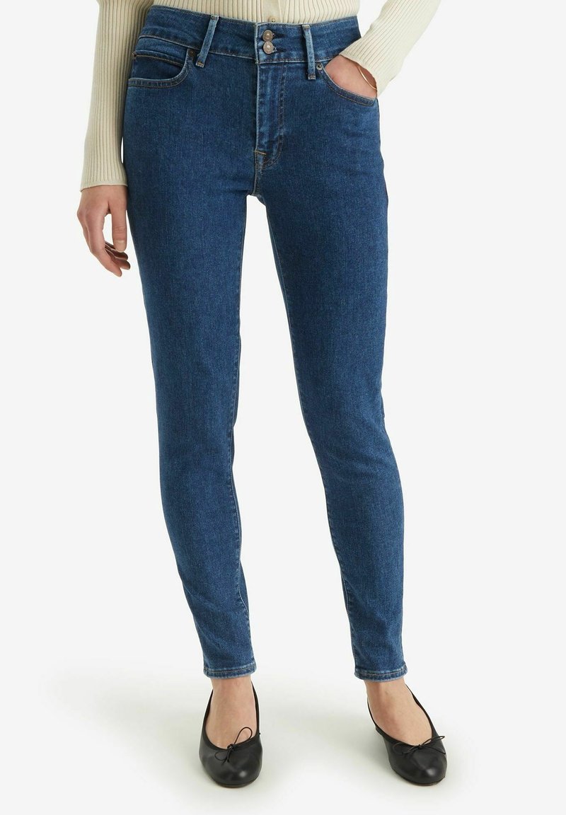 Vaqueros skinny azul de mezclilla con cintura alta, bolsillos frontales y cierre de botón. Textura suave con un diseño clásico.