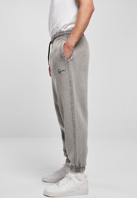 Šedé tepláky s elastickým pasem a šňůrkou, s postranními kapsami a elastickými lemy na kotnících. Černé logo na stehně.