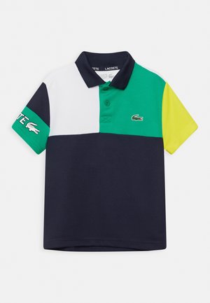 Polo shirt en color block bleu marine, blanc, vert et jaune, avec un col classique, deux boutons et un logo sur la manche. Confectionné en coton.