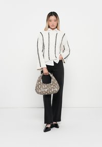 Witte gebreide trui met zwarte strepen, zwarte wijde broek, en een gestreepte beige handtas met een gebogen handvat. Zwarte platte schoenen maken de look af.