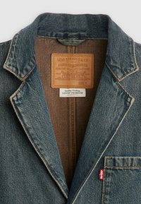 Cuello de chaqueta de mezclilla con etiqueta de parche de cuero de Levi Strauss & Co. y pequeña etiqueta roja de Levi's en el bolsillo del pecho, tamaño mediano.