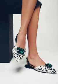 Ballerine slingback con punta affilata, caratterizzate da un motivo a spruzzi nero e bianco, un grande accento in pietra verde e un tacco piatto.