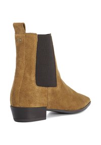 Brown suede ankle boot with elastic side panels, pointed toe, and a low stacked heel. Features a subtle gold logo accent on the heel.