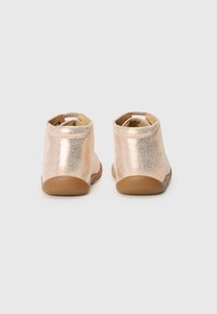 Botas de tobillo de cuero metálico rosa con un acabado texturizado, punta redondeada, apertura elástica y una suela de goma marrón flexible.