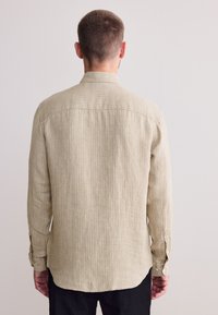 Camicia a righe beige a maniche lunghe con vestibilità rilassata, polsino con bottoni e orlo curvo. Tessuto strutturato con sottili linee verticali.