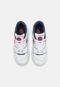 Sneakers in pelle bianca con accenti blu navy, logo New Balance rosso e cuciture grigie. Progettate con una chiusura lacci e linguetta imbottita.