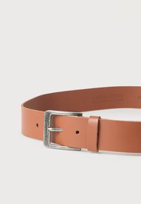 Καφέ δερμάτινη ζώνη με ασημί ορθογώνια αγκράφα χαραγμένη με "JACK & JONES", τοποθετημένη επίπεδα σε λευκή επιφάνεια.