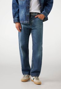 Jeans van denim in medium blauw met een relaxte pasvorm, met een lichte vervaging, vijf zakken en een knoopsluiting. Draagt samen met grijze sneakers.