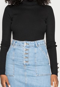 Un col roulé noir à côtes associé à une jupe en denim bleu clair taille haute dotée de cinq boutons sur le devant et de poches latérales.