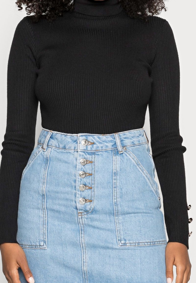 Un col roulé noir à côtes associé à une jupe en denim bleu clair taille haute dotée de cinq boutons sur le devant et de poches latérales.