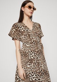 Robe imprimée léopard avec des manches courtes flottantes, un décolleté en V et une taille nouée. Le matériau semble lisse, dans des nuances de beige et de marron.