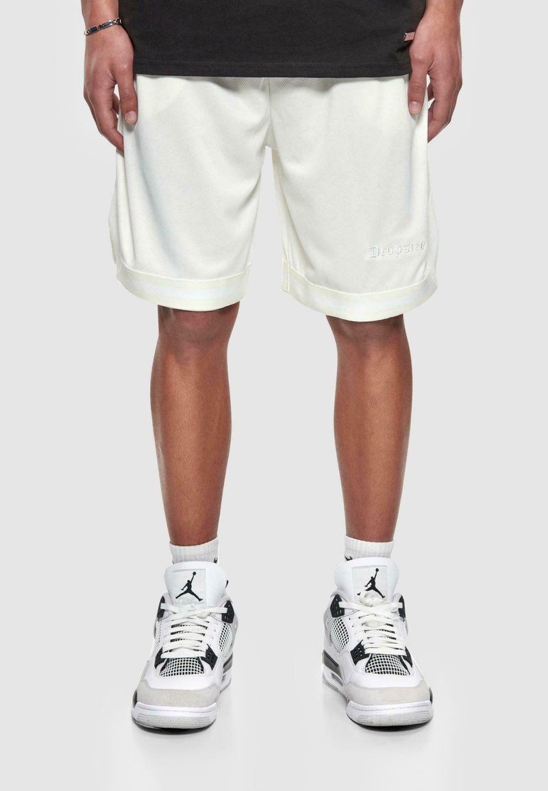 Hvide mesh shorts med opkrøllede kanter og broderet logo, parret med hvid- og sortfarvede sneakers med mesh-detaljer og logo-accenter.
