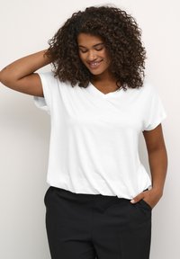 Vit V-ringad T-shirt gjord av mjukt tissu, avslappnad passform, korta ärmar och minimal detaljering, matchat med svarta byxor.