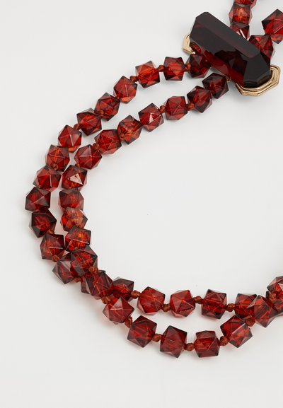 Collana di perle di cristallo rosso con forme esagonali facettate. Presenta una grande perlina angolare diaccento, infilata su un cordino marrone.