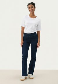 Witte T-shirt met korte mouwen, gecombineerd met donkerblauwe flared jeans. Sneakers met een witte basis en zwarte strepen. Eenvoudig en casual ontwerp.