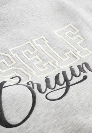 Hanorac gri cu litere albe brodate texturat "SELF" și "Origin" în scris de mână negru, evidențiind un contrast între materiale.