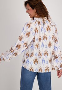 Langarmige blouse in het wit met een bruin en lichtblauw ruitpatroon, met eenGathered halslijn en mouwen, gecombineerd met blauwe jeans.