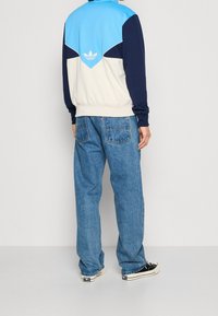 Blå, vit och marinblå färgblockerad zip-up jacka med ribbad fåll; kombinerad med löst sittande blå denimjeans och svarta sneakers.