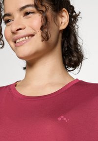 Maroon short-sleeved top with a round neckline, smooth texture, and a subtle dotted design on the chest.