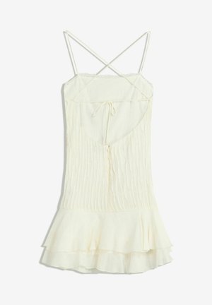 Robe couleur crème avec des bretelles fines croisées, un design texturé à côtes et un ourlet évasé à volants. Dispose d'un lien au dos et d'une fermeture éclair.