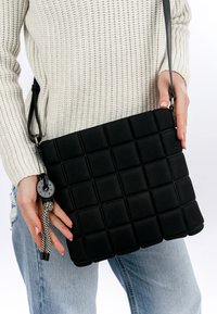 Borsa a tracolla nera realizzata in materiale testurizzato, con motivo a griglia, tracolla nera regolabile e un accento decorativo con clip.