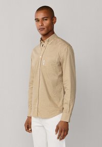 Camisa de manga larga y botón en un patrón a cuadros amarillo y marrón, hecha de una tela de textura suave, con un bolsillo en la parte frontal.