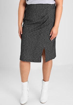 Kvinde iført en knælang sort-hvid mønstret nederdel med slids foran og hvide ankelstøvler på en ensfarvet baggrund.