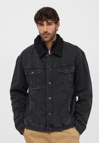 Giacca in denim nera con colletto in shearling nero testurizzato. Presenta chiusura con bottoni, tasche sul petto e un design con vestibilità ampia.