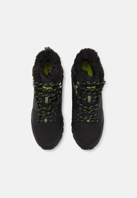 Black hiking boots with textured fur lining, neon green accents, and patterned shoelaces. Features a sturdy sole for traction and support.