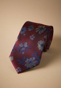 Cravate bordeaux avec un motif floral en bleu et or, dotée d'un tissu texturé et d'une extrémité effilée, roulée en forme de spirale.