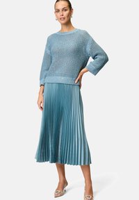 Maglione lavorato a maglia di un blu chiaro, con vestibilità ampia e maniche 3/4, abbinato a una gonna midi plissè di una tonalità coordinata per un look coeso.