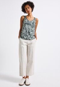 Zielono-białe top bez rękawów w wężowy wzór, luźny krój; w połączeniu z kremowymi spodniami w szerokim kroju i off-white sneakersami. Płaskie, gładkie tekstury.