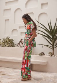 Barvna dvodelna obleka z cvetličnim vzorcem v zelenih, rdečih in oranžnih odtenkih. Kratka srajca z rokavi in široke hlače z žepi.