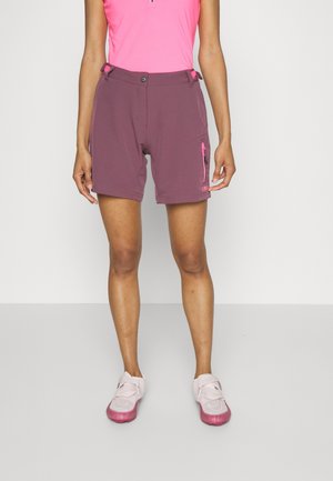 Person iført lilla outdoor-shorts med sidelomme med lynlås og pink atletisk top, kombineret med hvide og pink sportssko.