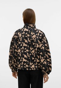 Gevoerde jas met zwarte achtergrond, bloemenpatroon in beige en roze, hoge kraag, elastische manchetten en een relaxte pasvorm.