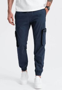 Pantalons cargo bleu marine avec des poignets élastiques, poches latérales zippées et un tissu texturé. Dotés d'une taille à cordon de serrage et d'une coupe décontractée.