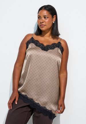 Kvinde med mellemtonet hudfarve og glat sort hår bærer en beige satin camisole med sort blondekant og små sorte prikker.