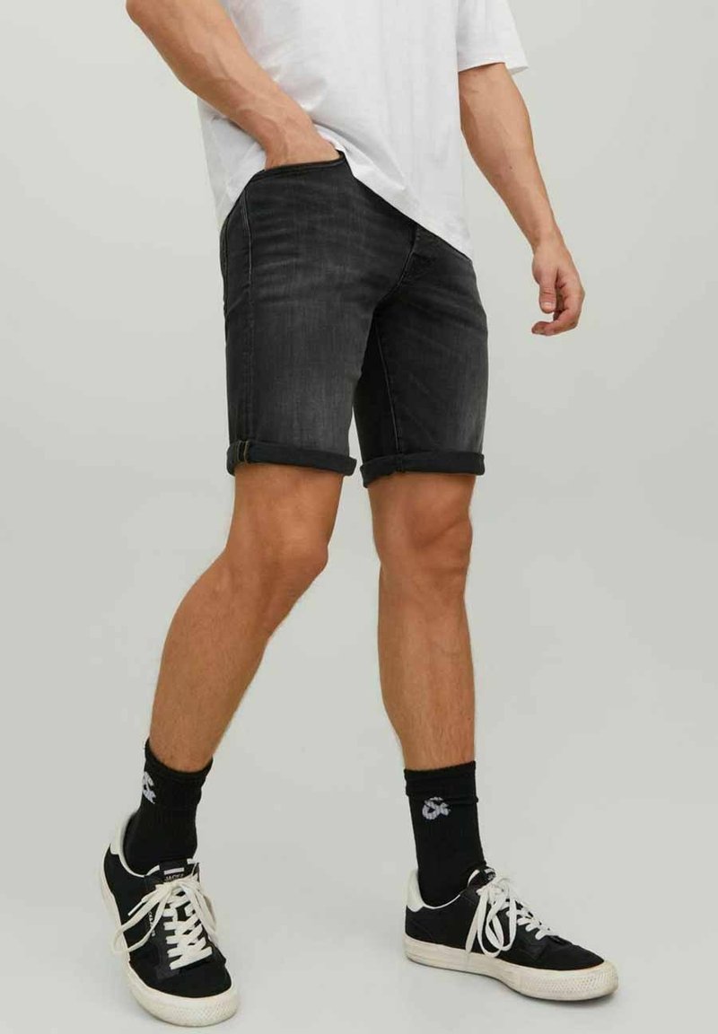 Shorts de mezclilla negra con los puños doblados, combinados con una camiseta blanca y zapatillas negras, que muestran un ajuste relajado y una textura suave.